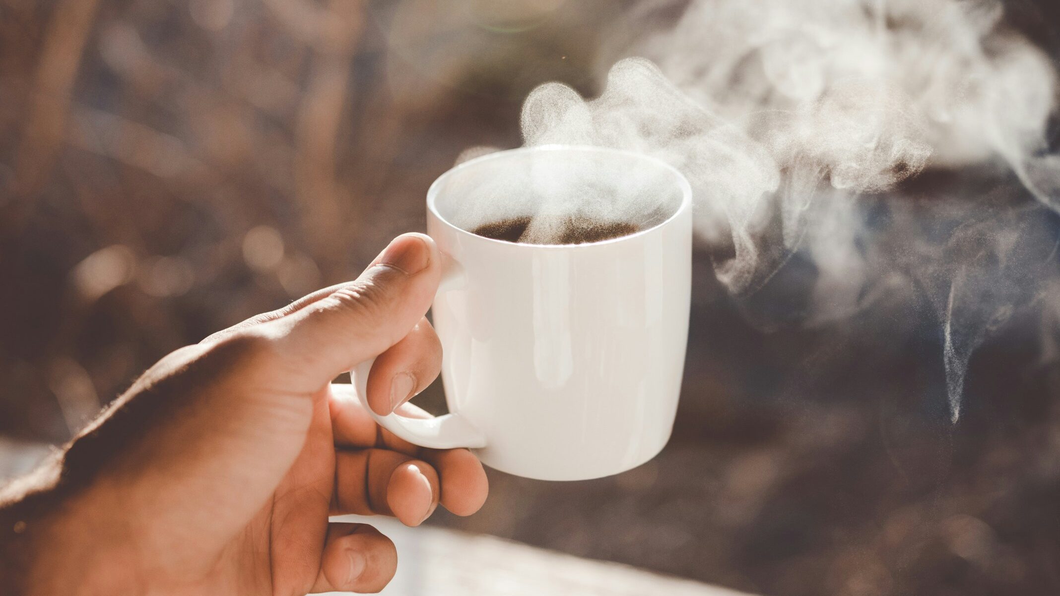 A hand holds a steaming cup of delicious coffee
