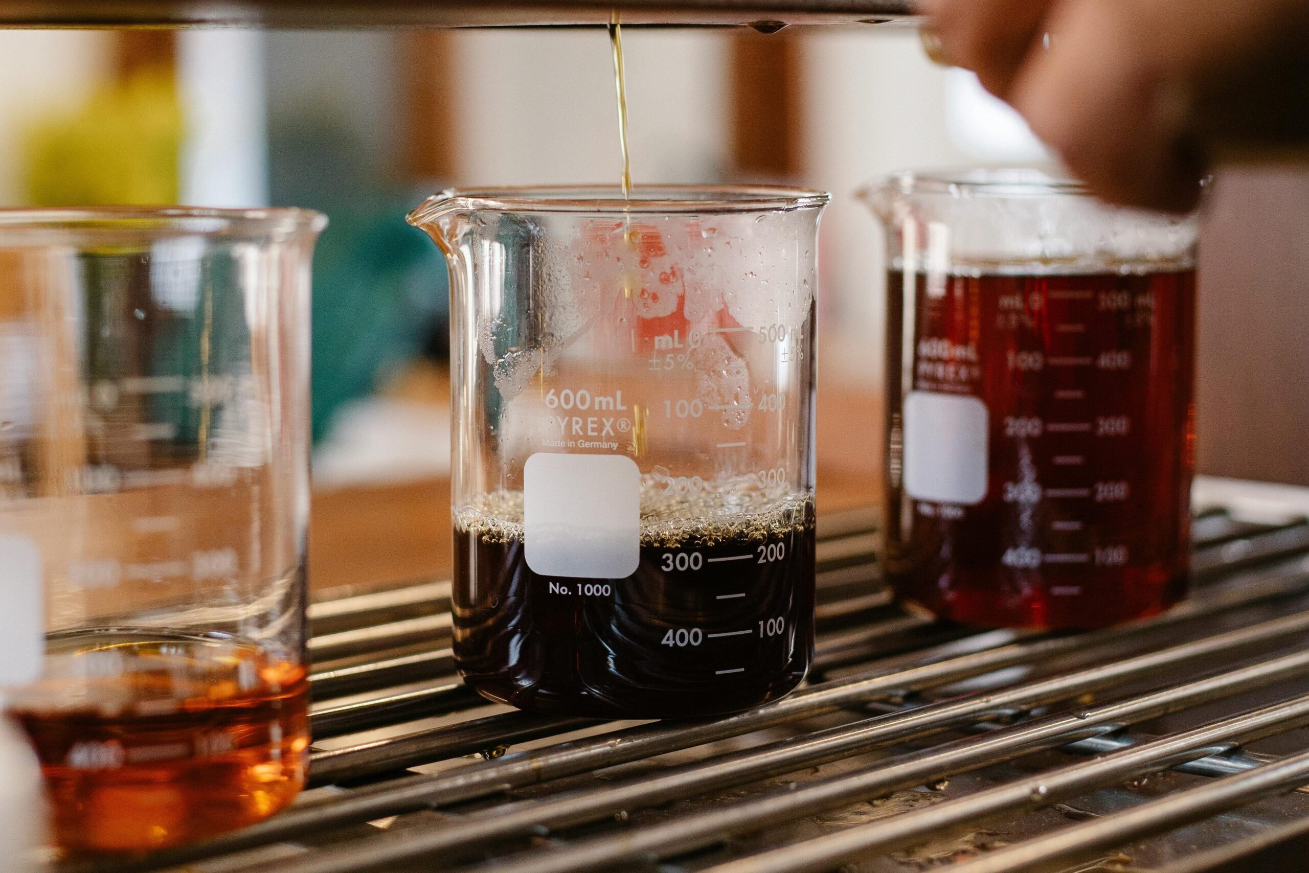 Three beakers of freshly brewed coffee, one light amber, one darker like syrup, and one nearly black, sit on a counter.